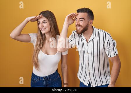 Ein junges Paar, das auf gelbem Hintergrund stand, war sehr glücklich und lächelte mit der Hand über den Kopf weit weg. Suchbegriff. Stockfoto