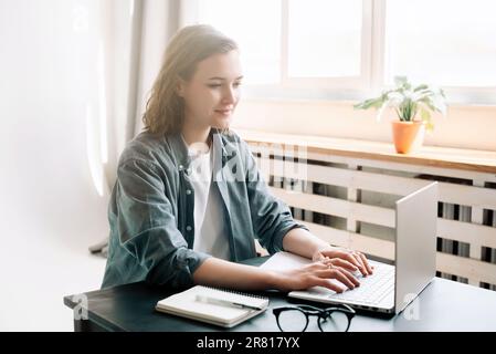 Junge Frau, die einen Laptop in einem modernen Büro verwendet, und Studentin, die bequem von zu Hause aus arbeitet. Online arbeiten, studieren, freiberuflich arbeiten Stockfoto