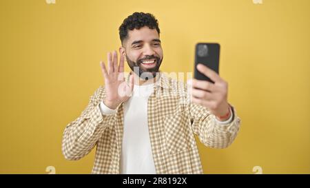 Junger lateinamerikanischer Mann, der selbstbewusst lächelt und Videoanrufe vor einem isolierten gelben Hintergrund führt Stockfoto