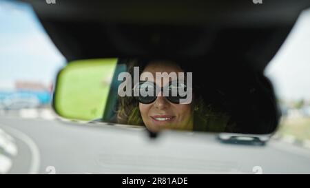 Eine hispanische Frau mittleren Alters, die Auto fährt und auf der Straße in den Rückspiegel schaut Stockfoto