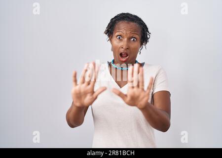 Afrikanische Frau mit Dreadlocks, die über weißem Hintergrund steht, verängstigt und verängstigt vor Angst Ausdruck, stoppt Geste mit Händen, schreit schockiert. Schwenken Stockfoto
