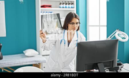 Eine junge, wunderschöne hispanische Ärztin, die sich Röntgenbilder mit einem Computer ansieht, der in der Klinik steht Stockfoto