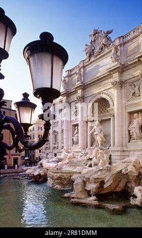 Trevi-Brunnen Rom mit Statuen und Wasserfällen mit traditionellen Straßenlaternen im Vordergrund bei warmem Glühen Sonnenuntergang Rom Italien Wahrzeichen Porträt vertikaler Sonnenuntergang Trevi-Brunnen Fontana di Trevi Rom Italien Stockfoto