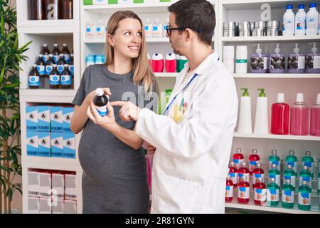 Mann und Frau, Apotheker und schwangere Klientin, die in der Apotheke eine Medikamentenflasche halten Stockfoto