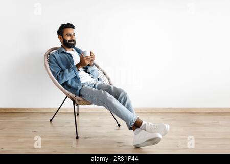 Ein Araber trinkt heißen Kaffee im Sessel an der weißen Wand Stockfoto