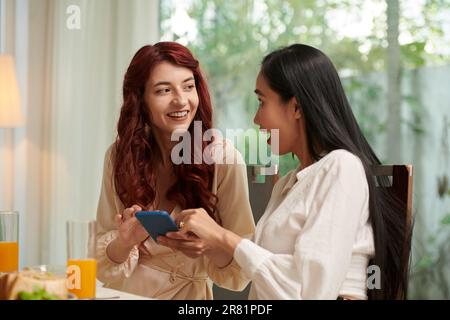 Aufgeregte junge Frau, die ein Foto eines Freundes auf einer Dinnerparty zeigt Stockfoto