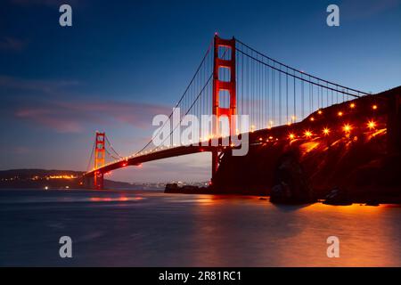 Ein spektakulärer Blick auf die Golden Gate Bridge, beleuchtet am Nachthimmel, spiegelt sich im stillen Wasser unter Ihnen Stockfoto