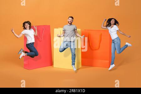 Aufgeregte multiethnische Millennials, die vor riesigen Einkaufstaschen springen Stockfoto