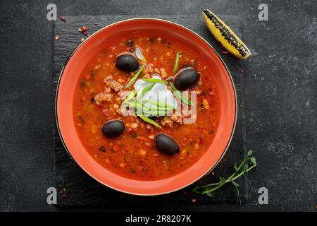 Ukrainische Suppe solyanka mit Fleisch, Oliven, Sauerrahm, Kräutern und Zitrone Stockfoto