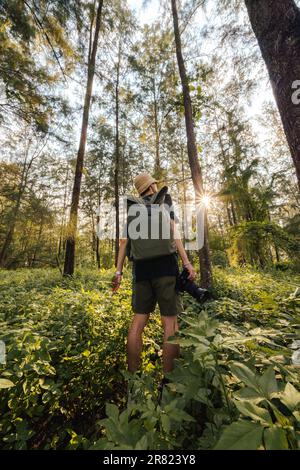 Ein junger erwachsener Mann steht in einem üppigen Wald und trägt einen grünen Gaston Luga Rucksack Stockfoto