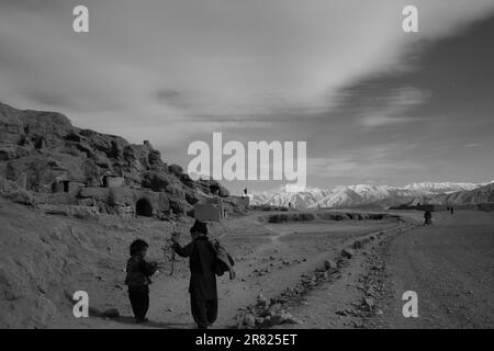 Eine Graustufenaufnahme von zwei Menschen, die in einer kargen Wüstenlandschaft in Afghanistan spazieren Stockfoto