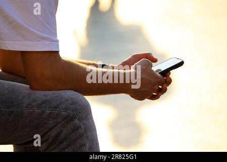 Smartphone in den Händen eines Mannes, der im Sonnenlicht auf einer Straße sitzt. Telefon im Freien, mobile Kommunikation Stockfoto