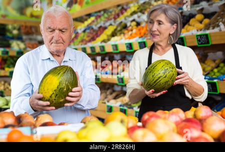 Dame im Gemüsehändler hilft dem alten Mann, Melone zu wählen Stockfoto