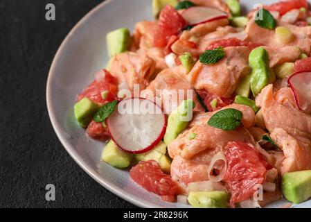 Chilenischer Lachs seviche mit Grapefruit, Avocado, Rettich, Zwiebel und Minze auf einem Teller mit Gabel auf schwarzem Hintergrund. Schließen Stockfoto