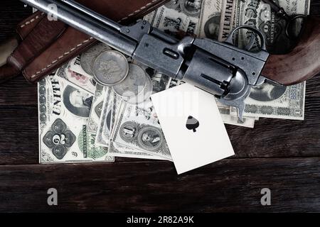 Alte Westwaffe. Colt Revolver, Pik-Messer, Karten auf Papier und Silberdollar-Haufen an Deck. Stockfoto