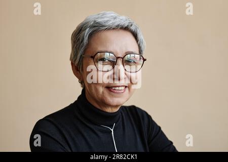 Hüftbild einer modernen asiatischen Seniorin, die in die Kamera schaut und eine Brille trägt Stockfoto