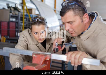 Weibliche und männliche Arbeiter beim Schneiden von Metallprofilen in der Werkstatt Stockfoto