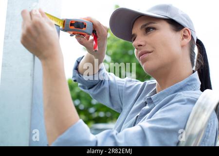 Eine Frau auf einer Trittleiter, die ein Maßband benutzt Stockfoto