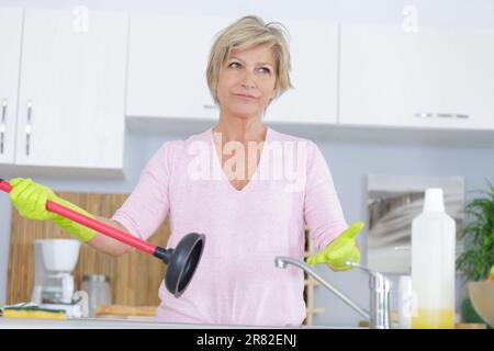 Frustrierte, reife Frau, die einen Waschbeckenkolben in der Hand hält Stockfoto