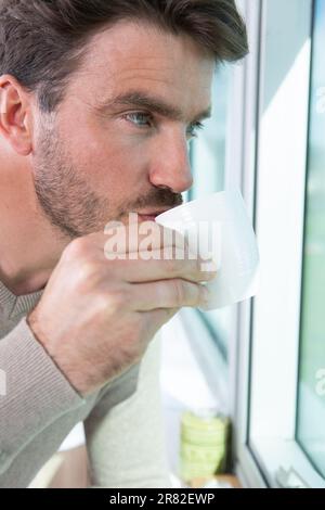 Rücksichtsvoller Mann mit Kaffeetasse, der durch das Fenster schaut Stockfoto