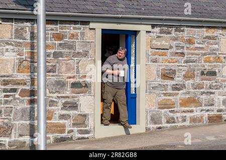 18. Juni 2023 Cullen, Moray, Schottland. Das ist ein Mann, der vor seiner Tür steht und die Sonne mit einer Tasse Tee aufsaugt. Stockfoto