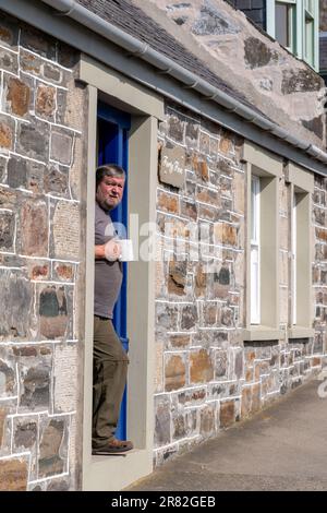 18. Juni 2023 Cullen, Moray, Schottland. Das ist ein Mann, der vor seiner Tür steht und die Sonne mit einer Tasse Tee aufsaugt. Stockfoto