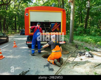 Kanalisationsarbeiter, die den Gullyschacht reinigen und die Kanalisation auf der Straße freimachen Stockfoto