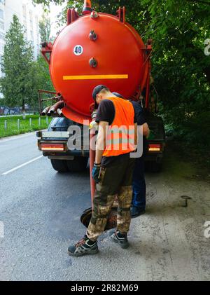 Kanalisationsarbeiter, die den Gullyschacht reinigen und die Kanalisation auf der Straße freimachen. Stockfoto