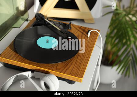 Eleganter Plattenspieler mit Vinylscheibe und Kopfhörern auf weißer Kommode zu Hause Stockfoto