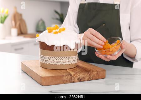 Frau dekoriert köstlichen Osterkuchen mit getrockneten Aprikosen auf einem weißen Marmortisch in der Küche, Nahaufnahme Stockfoto