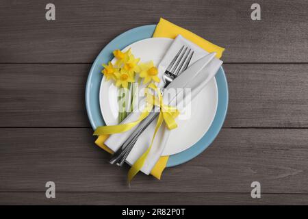 Festlicher Tisch mit Narzissen und Besteck auf Holzhintergrund, Draufsicht. Osterfeier Stockfoto