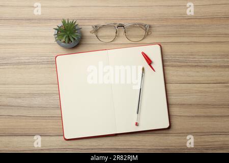 Kugelschreiber, Notizbuch und Brille auf Holztisch, flach liegend Stockfoto