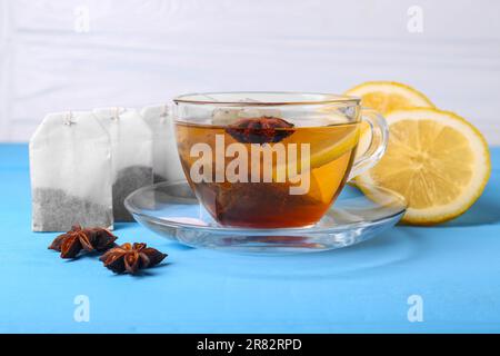 Teebeutel, eine Tasse heißes Getränk, Anissterne und Zitrone auf einem hellblauen Holztisch Stockfoto