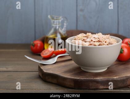 Schüssel mit Thunfischkonserven und Tomaten auf Holztisch, Platz für Text Stockfoto