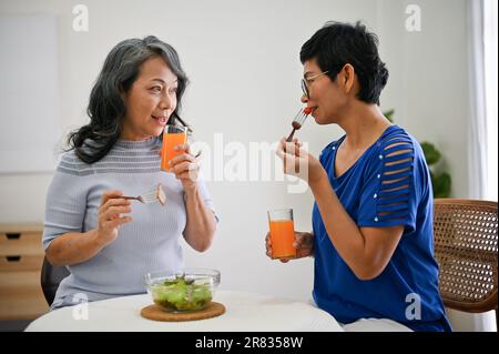 Zwei reizende und glückliche, im Ruhestand befindliche asiatische Freundinnen genießen ihren gesunden Brunch und plaudern im Speisesaal und verbringen Zeit an der Woche Stockfoto