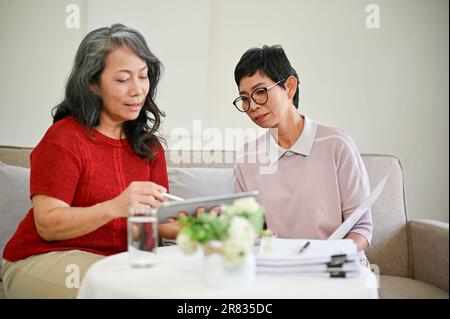 Eine schöne, reife asiatische Krankenversichererin mittleren Alters besuchte eine Rentnerin zu Hause, um Geschäfte zu machen. Stockfoto