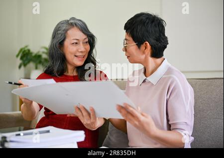 Eine schöne und professionelle asiatische Krankenversichererin mittleren Alters besuchte eine Rentnerin zu Hause, um einen Versicherungsvertrag abzuschließen. Stockfoto