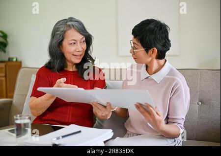 Eine professionelle asiatische Krankenversichererin mittleren Alters besuchte eine Rentnerin zu Hause, um einen Versicherungsvertrag abzuschließen und die Versicherung zu prüfen Stockfoto