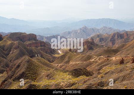 Luftaufnahme von drohne von Binggou Danxia Canyon Relief in Zhangye, Sunan Region, Provinz Gansu, China. Scharfe Spitzen Spitzen im Geopark. Straße auf V Stockfoto