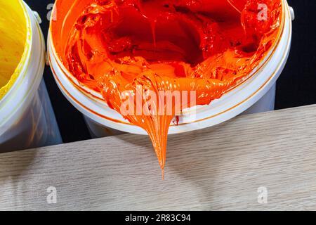 Orangefarbene Farbe tropft aus dem weißen Schaft. Plastisoltinte wird zum Bedrucken von Textilien verwendet, da sie langlebig, leicht aushärtend und dehnbar ist Stockfoto