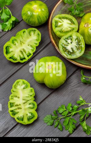 Ganze grüne und gehackte Tomaten auf dem Tisch. Flach verlegt. Dunkler Holzhintergrund. Stockfoto