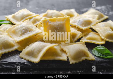 Rohe Ravioli mit Mehl und Basilikum auf dunklem Hintergrund, frische italienische Ravioli Stockfoto