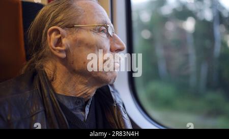 Nahaufnahme des Seniors mit Brille fährt in einem Zug und blickt aus dem Fenster Stockfoto