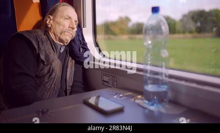 Nahaufnahme des Seniors mit Brille fährt in einem Zug und blickt aus dem Fenster Stockfoto