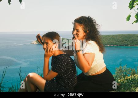 Mutter flechtet die Zöpfe ihrer Tochter und sieht sie an. Das Meer im backgroundю-Kinobild Stockfoto