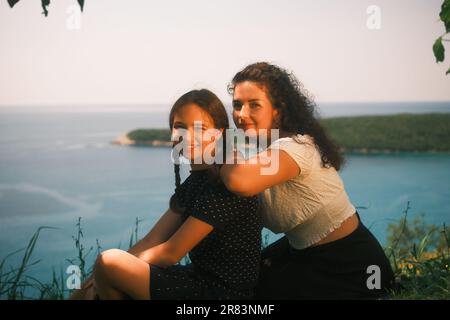 Mutter und Tochter sitzen auf dem Gras und lächeln und schauen auf die Kameralinse Stockfoto