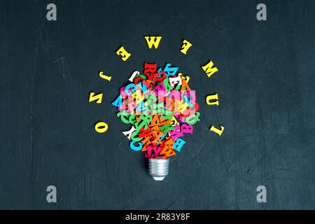 Mehrfarbige hölzerne Buchstaben, die in einem leuchtenden Glühbirnensymbol auf einem Hintergrund an der Tafel angeordnet sind. Kreatives Bildungs- und Inspirationskonzept. Stockfoto