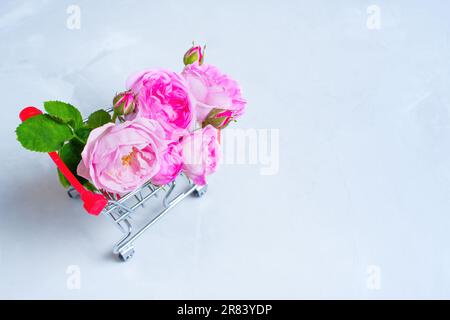 Nahaufnahme eines zarten, blühenden Rosenstraußes in einem Miniaturwagen isoliert auf grauem Hintergrund. Kosmetische Hintergründe. Stockfoto