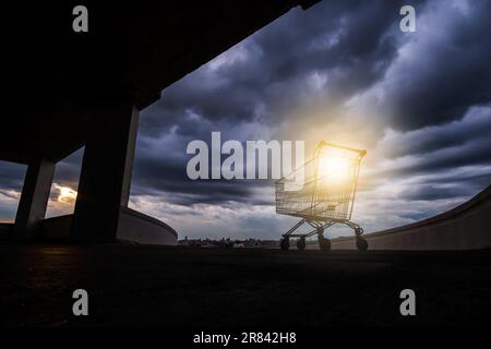 Ein Einkaufswagen auf einem Parkplatz auf dem Dach eines verlassenen Einkaufszentrums, der Sonnenuntergang durch Regenwolken im Hintergrund. Stockfoto