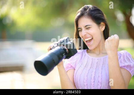 Aufgeregter Fotograf in einem Park, der die Ergebnisse mit einer spiegellosen Kamera überprüft Stockfoto